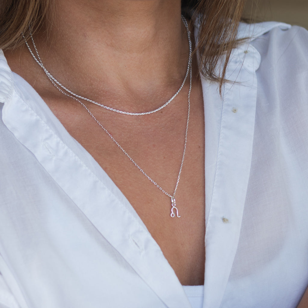 An image of a woman with light hair wearing a silver zodiac sign necklace, featuring a pendant of the astrological symbol for a specific zodiac sign, hanging from a delicate chain.