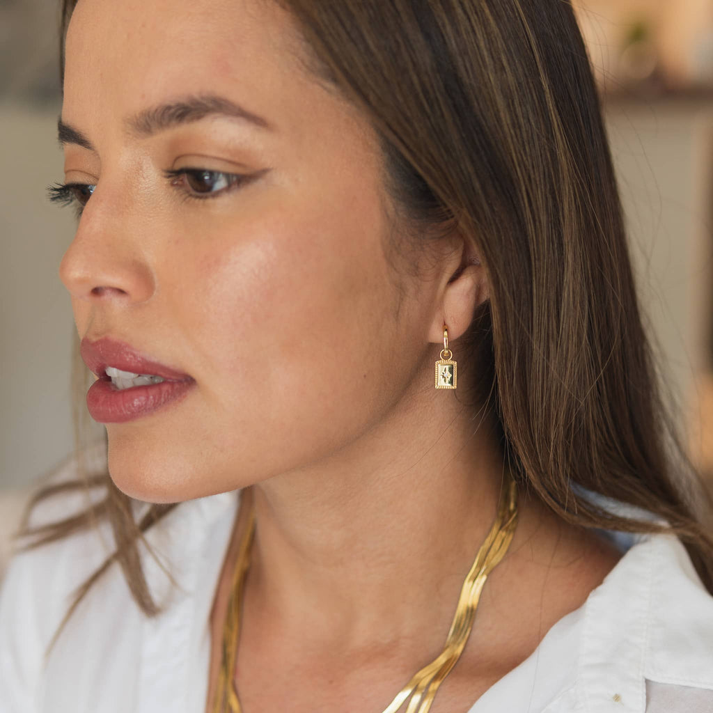 Woman wearing Gold Rectangle Drop Earrings with Starburst Design