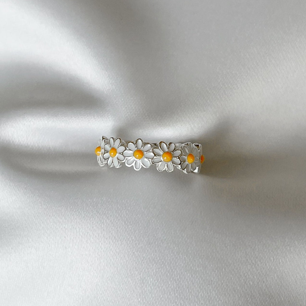 A delicate flower ring with vibrant white petals and a yellow center, crafted from shiny silver metal.  The ring comes in a range of sizes to ensure the perfect fit, and is suitable for any occasion, from casual to formal.